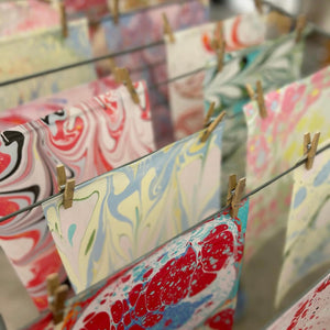 Load image into Gallery viewer, ROCWORX Marbling pattern papers pegged up to dry at a workshop