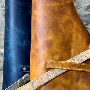 Load image into Gallery viewer, Close up detail of Italian veg tanned leather aprons in Giallo (mustard yellow) and  Acqua (Dark Teal).  Hand stitched branded chef's towel slot, abstract marbling pattern hand-stitched lined ties