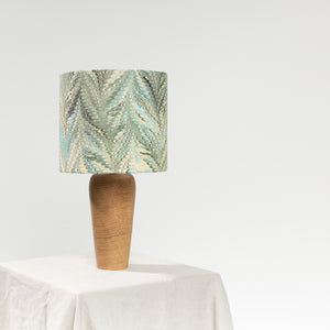 Load image into Gallery viewer, Lamp unlit, sitting on a natural linen tablecloth with a white background.  Linen lampshade in Feathers Nonpareil marbling pattern in dark green and lemon, with hint of teal.  On a wooden base
