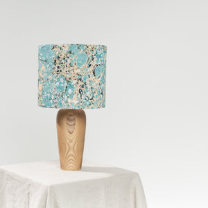 Load image into Gallery viewer, Lamp, unlit, sits on natural linen tablecloth, against a white background.  Marbled cotton lampshade in Stone marbling pattern in dark teal and soft lemon, hint of black.  Vase style wooden base turned on Dartmoor
