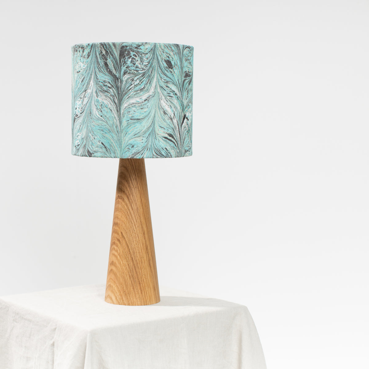 Linen lampshade on Oak wooden base on a linen table top and white background.  Marbling Chevron pattern in teal and dark green.
